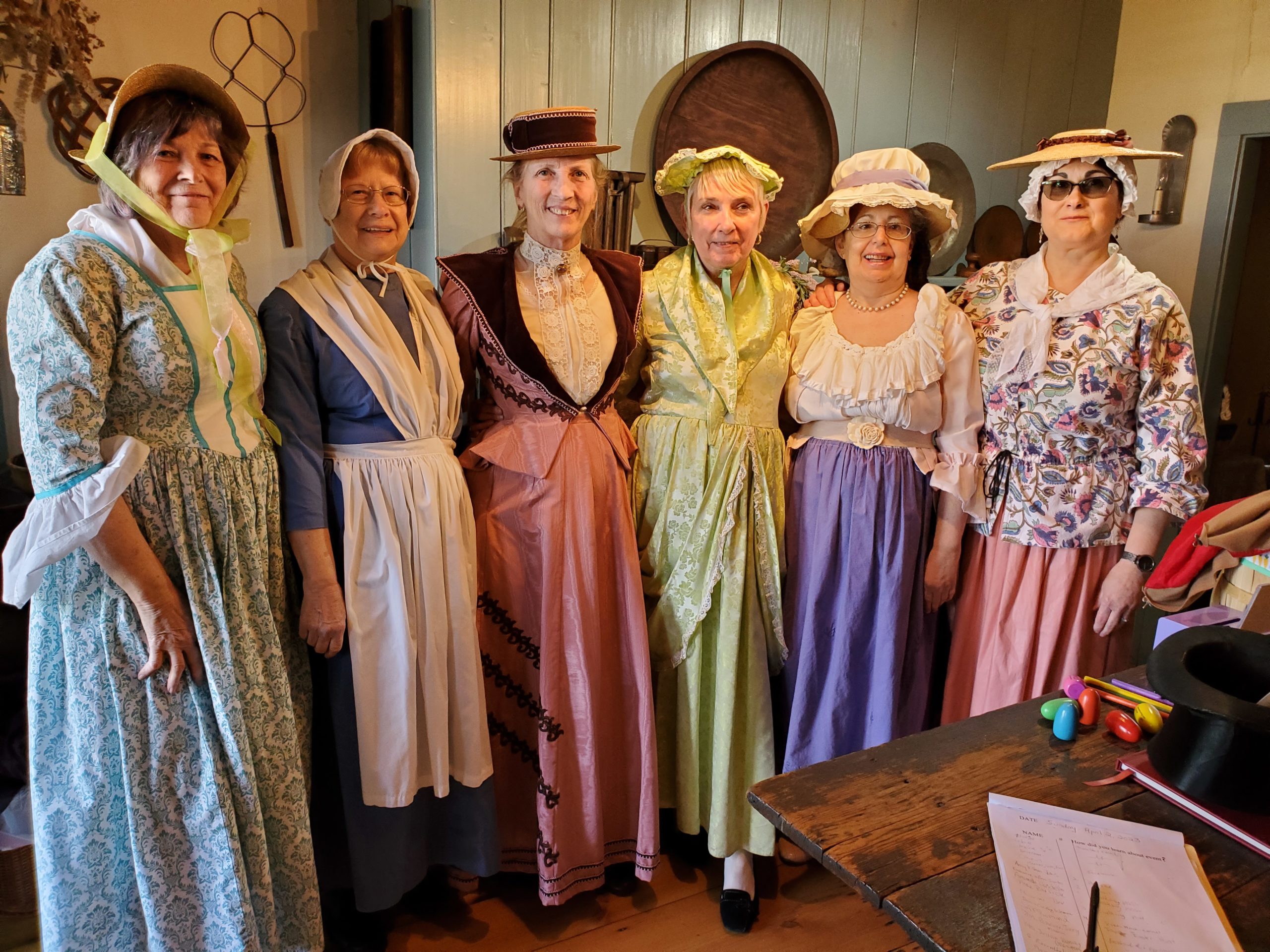 Six ladies dressed in 18th and 19th century fashions in the kitchen of the Osborn Cannonball House Museum